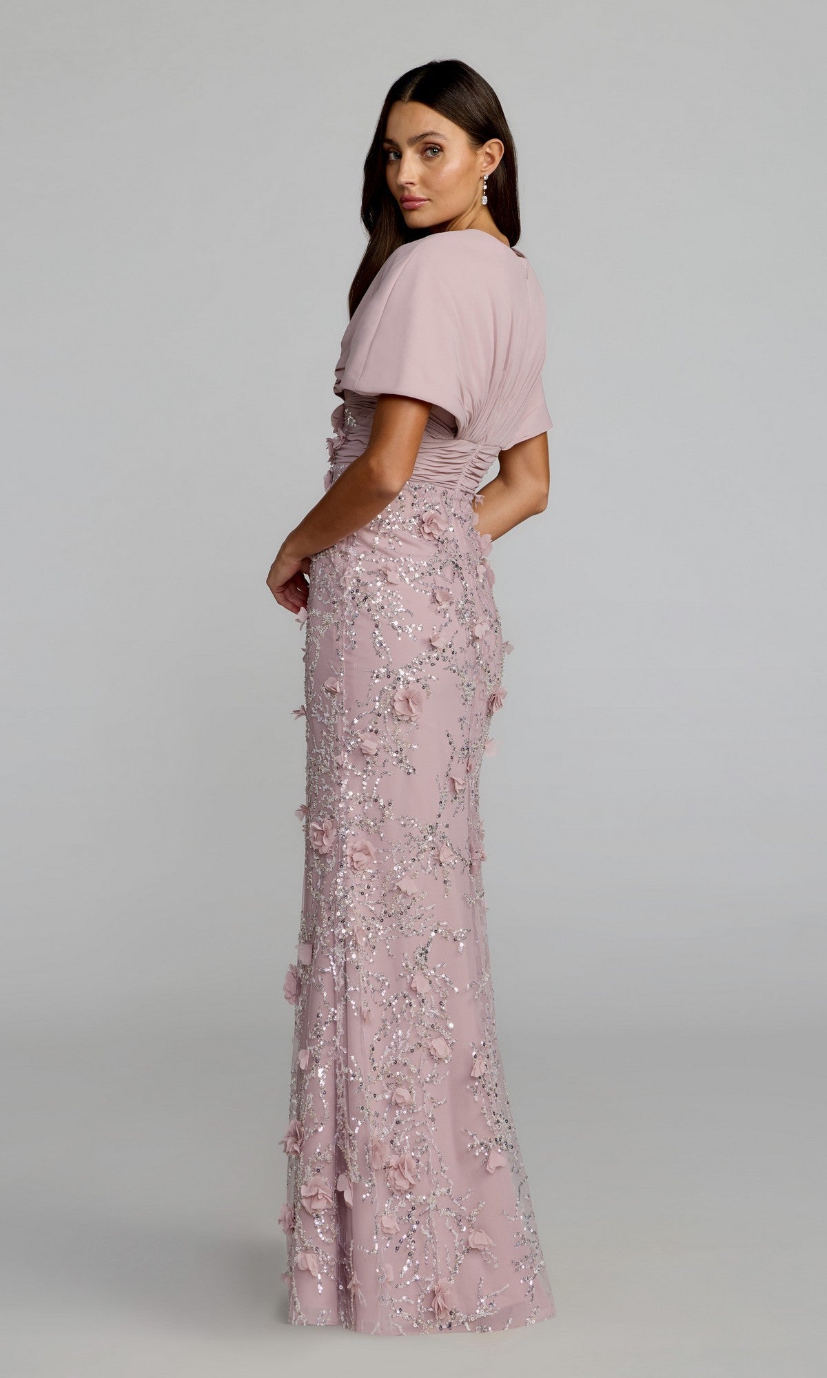 A woman wearing the Mac Duggal 69125 long formal dress—a floor-length light pink evening gown with short sleeves and floral sequin embellishments, featuring an elegant v-neck chiffon bodice—stands against a plain background.